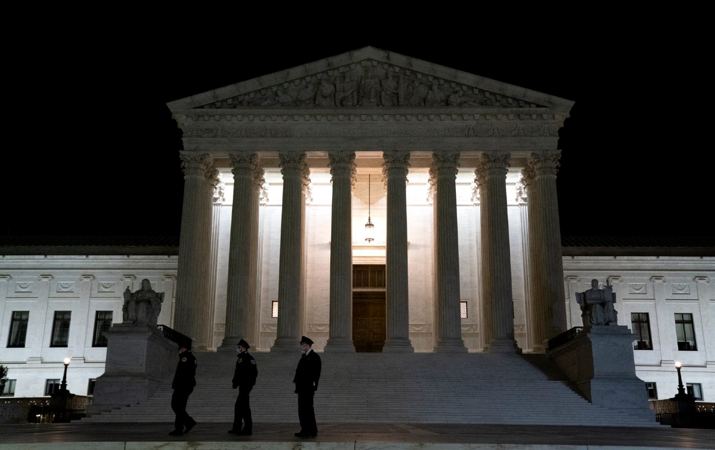 Three police officers stand outside the Supreme Court building at night