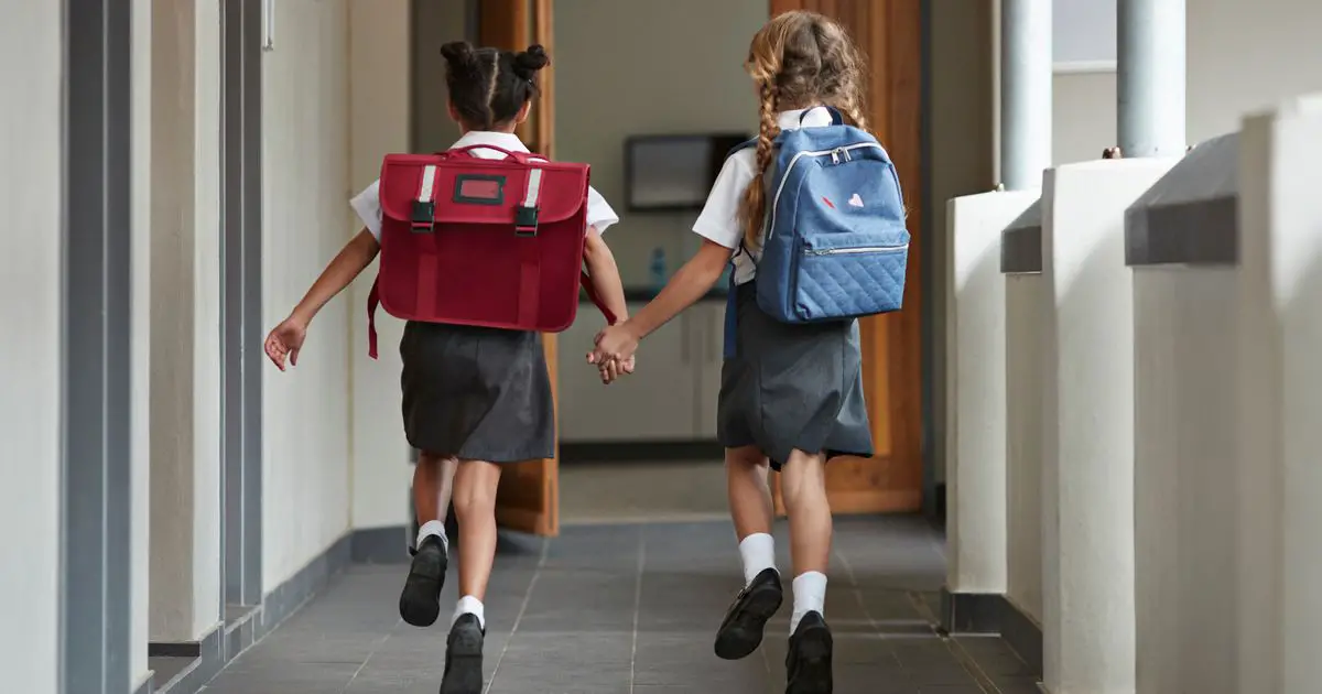 Two school girls running through a school hall holding hands