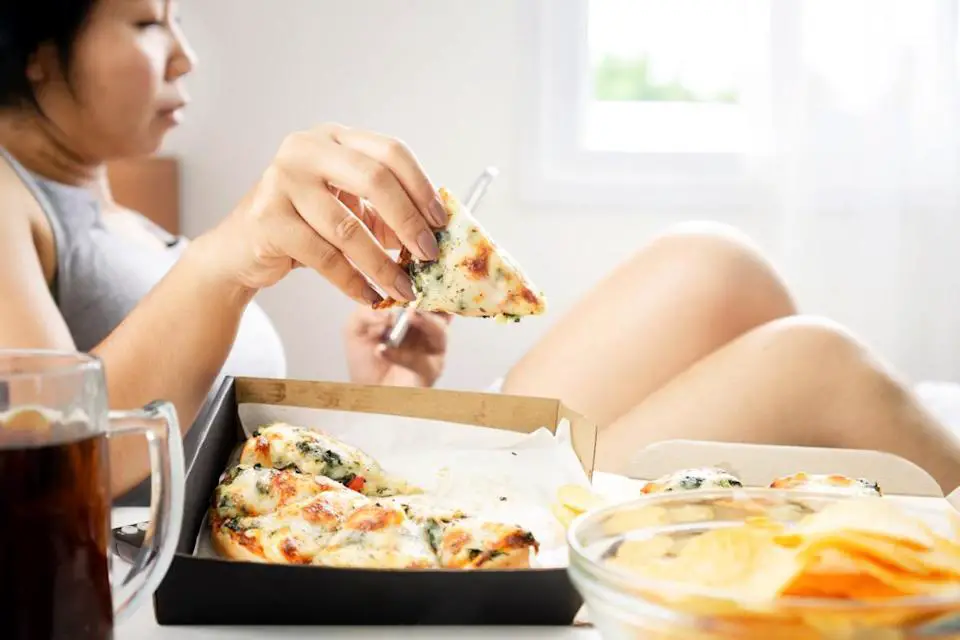 woman eating pizza in bed