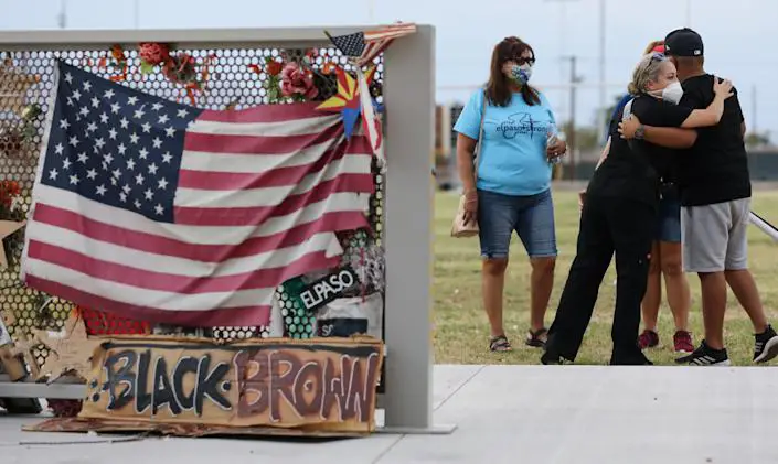 People embrace at a temporary memorial in a Texas park.