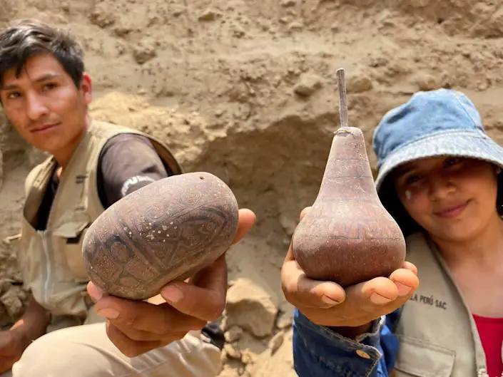 Archeologists hold up ceramic posts found in a tomb in Cajamarquilla, Peru.