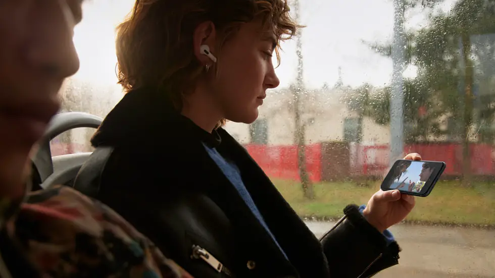 Girl on a bus with AirPods on watching a video with SharePlay using 5G on iPhone SE.